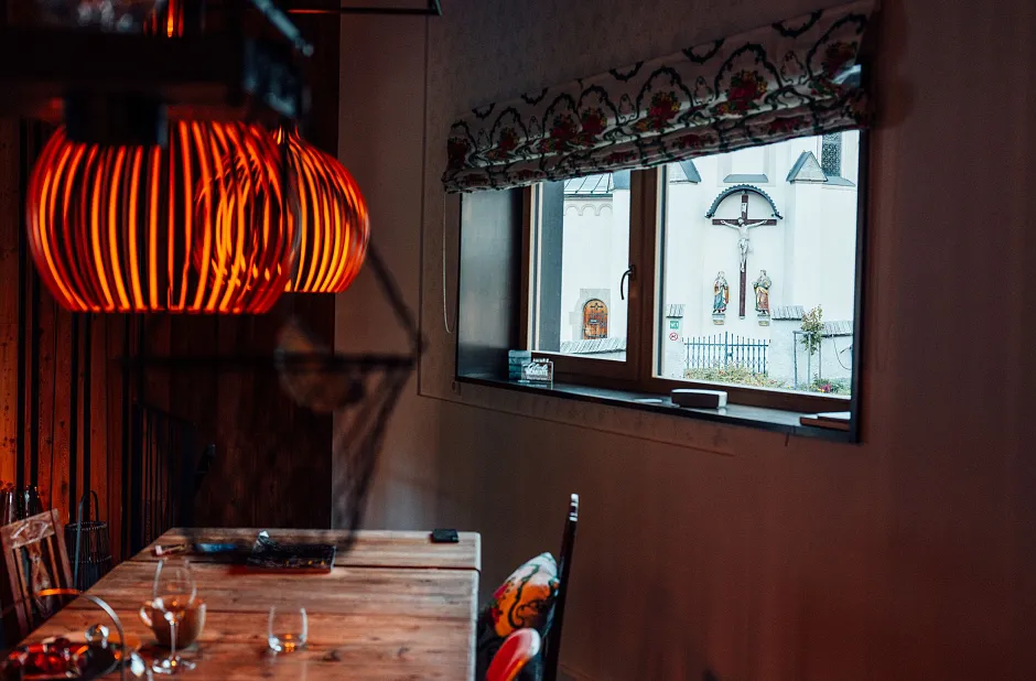 Gemütliches Esszimmer mit Holz-Esstisch, dekorativen orange leuchtenden Hängelampen und Fenster mit Blick nach draußen.